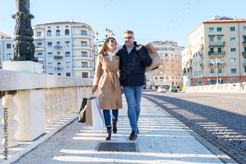 Fashionable couple joyfully shopping in the city of Verona, walking with bags in the sunshine, embracing style and love, making lasting memories