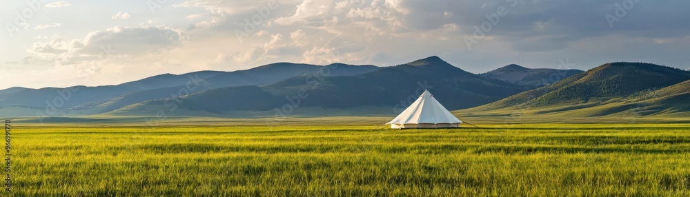 Fototapeta premium A serene landscape featuring a white tent surrounded by lush green fields and distant mountains under a clear blue sky.