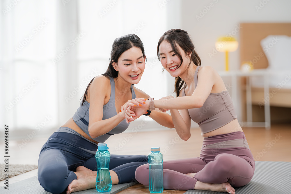 Two Asian women looking at smartwatches to measure their physical fitness during a break from exercise, health and wellness concept, exercise
