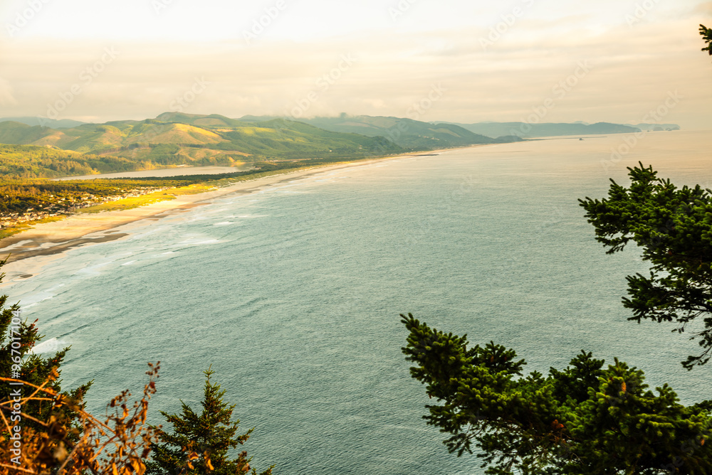 Obraz premium Aerial view of the Oregon coast with mountains and a beach at sunset.