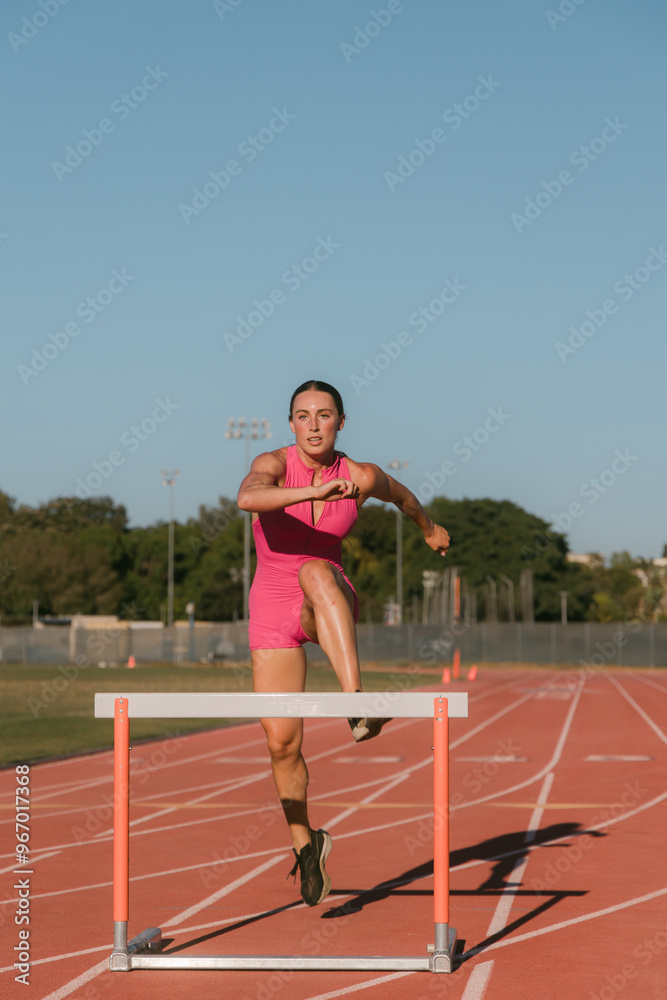 Obraz premium Female track athlete about to go over hurdle on track