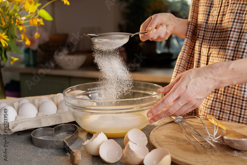 Εκτύπωση καμβά Close-up of female hands sifting flour and preparing dough in a transparent bowl against the background of a kitchen