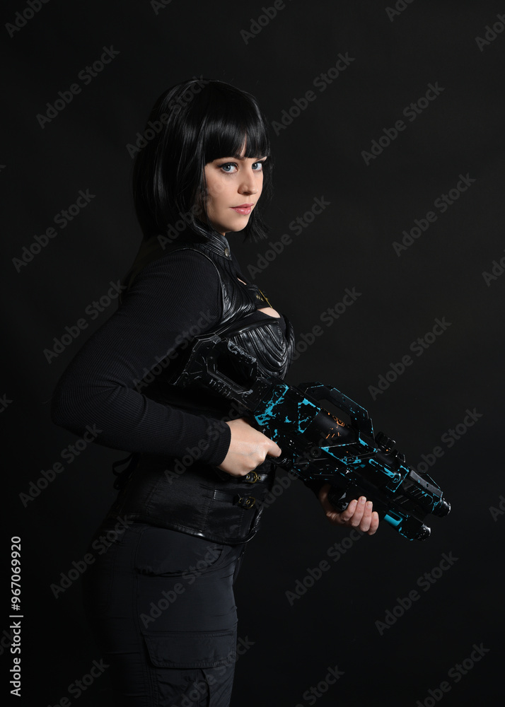 Naklejka premium Close up portrait of beautiful black female model wearing black sci fi futuristic dystopian leather bodysuit costume. holding gun weapon. isolated dark studio background moody silhouette.