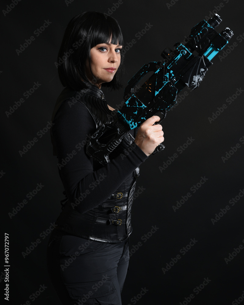 Naklejka premium Close up portrait of beautiful black female model wearing black sci fi futuristic dystopian leather bodysuit costume. holding gun weapon. isolated dark studio background moody silhouette.