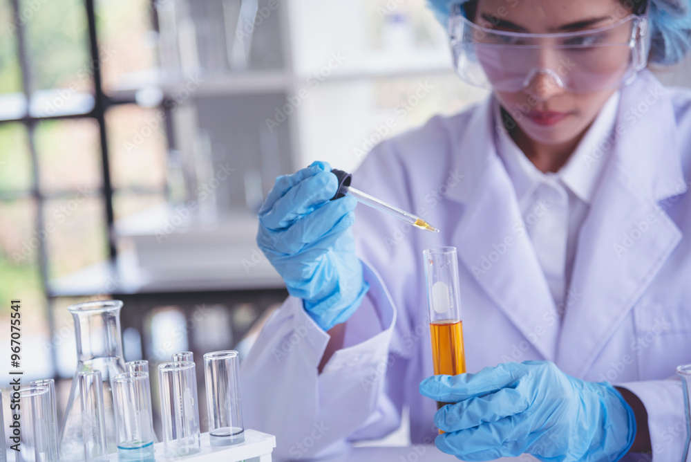 Scientist woman holding chemical test yellow glass tube testing science laboratory. Lab technician holding gold fluid drop to glass tube Urine sample. Asian woman scientist working medical chemistry Scientist woman holding chemical test yellow glass tube testing science laboratory. Lab technician holding gold fluid drop to glass tube Urine sample. Asian woman scientist working medical chemistry