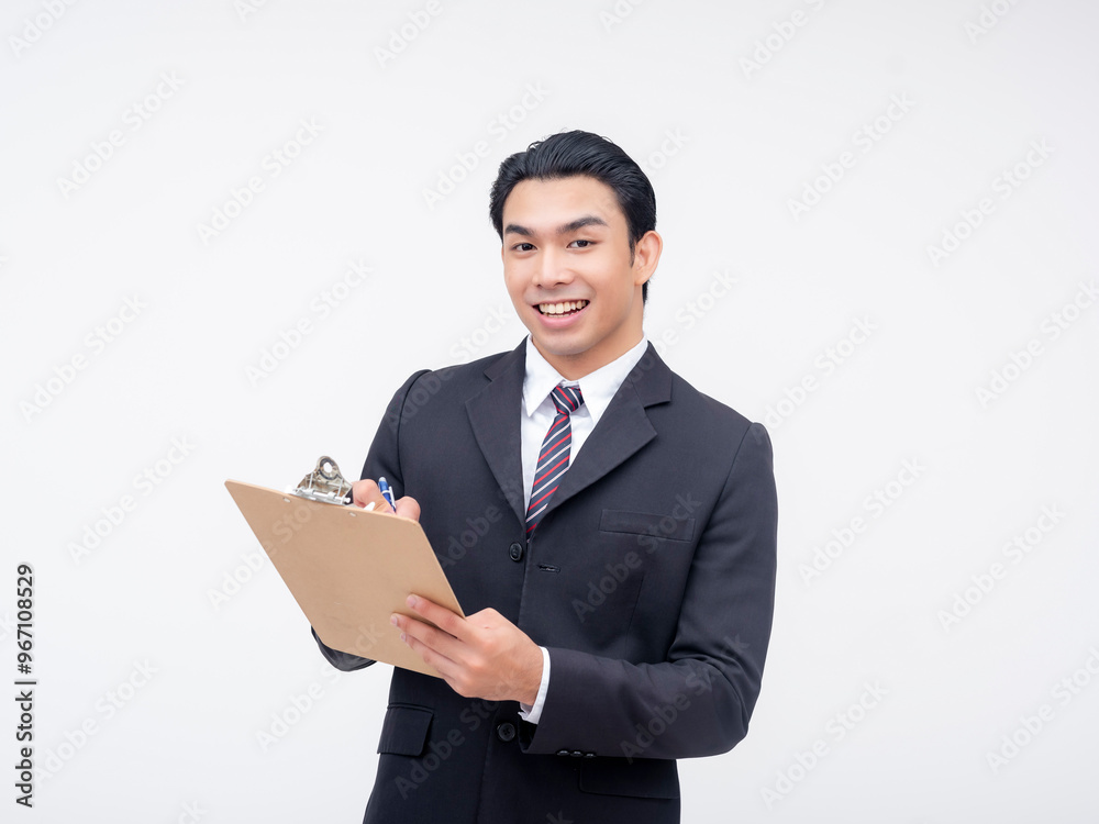 A young upbeat asian executive smiling while jotting down notes on a clipboard. Isolated on a white background.