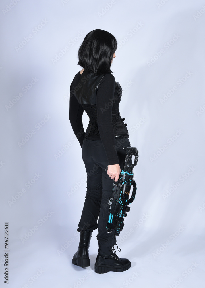 Naklejka premium Full length portrait of beautiful black female model with short black hair wearing sci fi futuristic dystopian leather bodysuit costume. Standing walking pose, isolated white studio background.