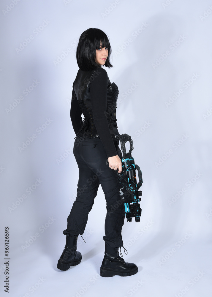 Naklejka premium Full length portrait of beautiful black female model with short black hair wearing sci fi futuristic dystopian leather bodysuit costume. Standing walking pose, isolated white studio background.