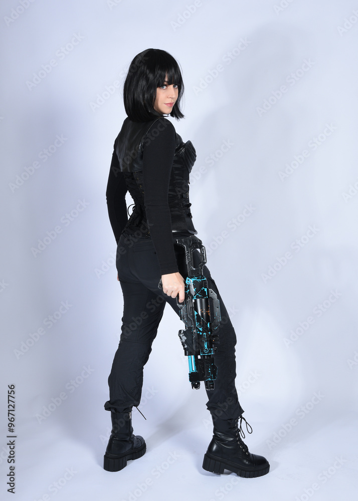 Naklejka premium Full length portrait of beautiful black female model with short black hair wearing sci fi futuristic dystopian leather bodysuit costume. Standing walking pose, isolated white studio background.
