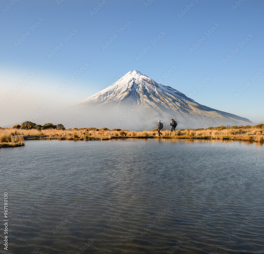 Couple hiking Pouakai circuit. Snow-capped Mt Taranaki in the background. New Zealand.