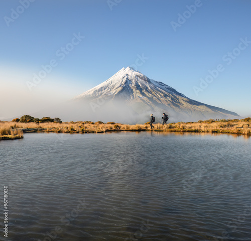 Obraz na płótnie Couple hiking Pouakai circuit. Snow-capped Mt Taranaki in the background. New Zealand. w salonie