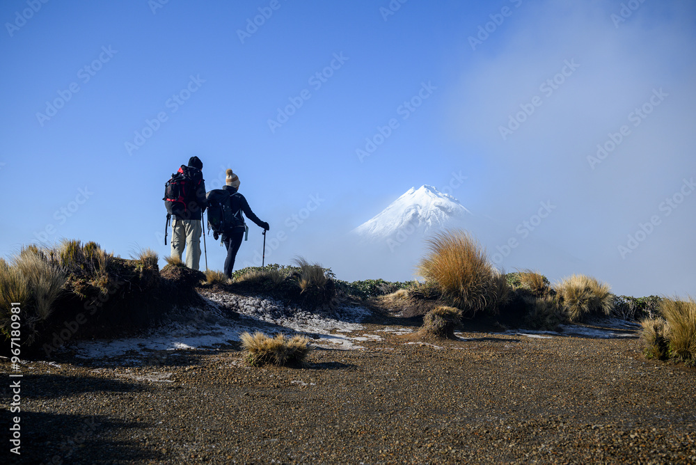 Couple looking at Snow-capped Mt Taranaki in the clouds. Pouakai Circuit track. New Zealand.