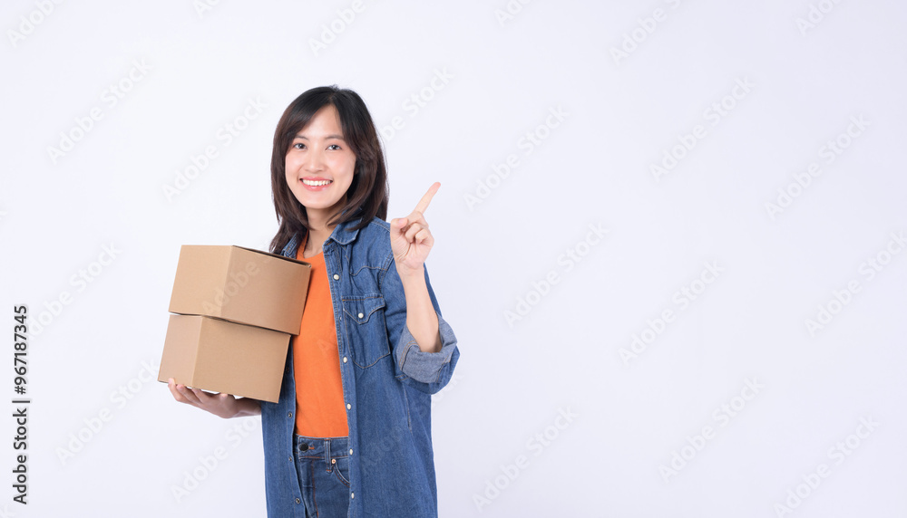 Portrait young asian woman wearing orange t-shirt and denim shirt holding parcel box isolated on white studio background, Delivery courier and shipping service concept. Portrait young asian woman wearing orange t-shirt and denim shirt holding parcel box isolated on white studio background, Delivery courier and shipping service concept.