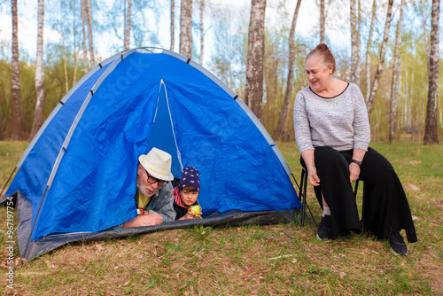 Grandma, grandpa and grandson are relaxing in a tourist tent in the forest. Active family recreation.