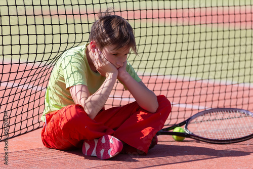 The boy lost the tennis competition. The child sits at the net with a racket. Psychology of sports in childhood.