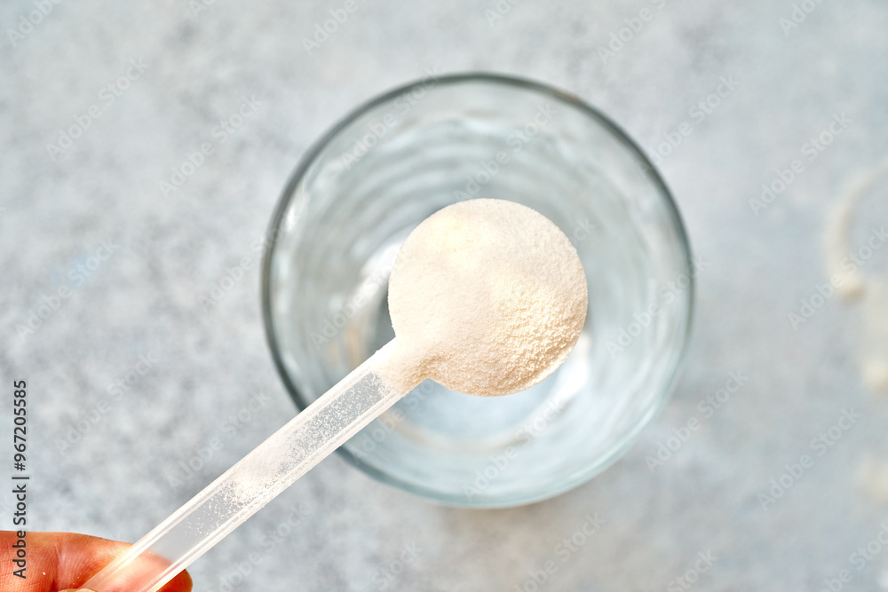 Collagen powder in a plastic measuring spoon above a glass cup of water, top view
