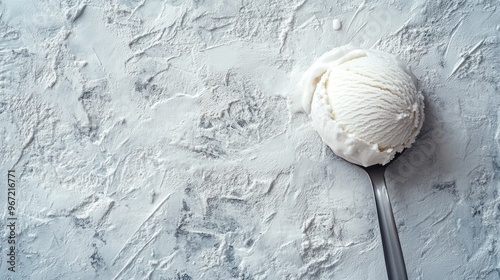 A single scoop of white vanilla ice cream on a metal spoon sits on a textured grey background.