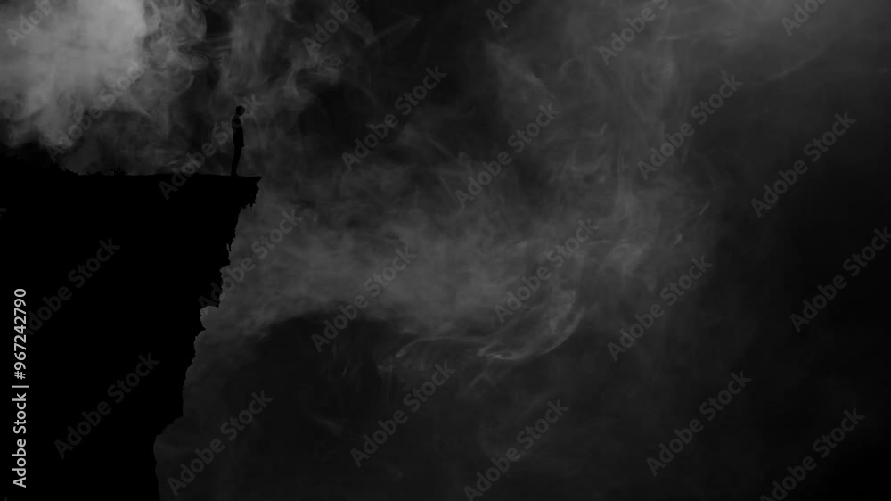 Dark Silhouette of a Person Standing on the Edge of a Cliff Backlit With Fog