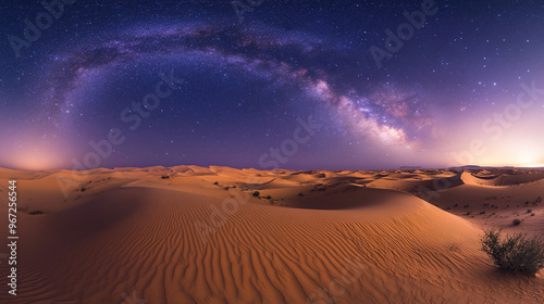 A starry night sky with the Milky Way visible above the desert landscape and sand dunes glowing in the faint glow of starlight.