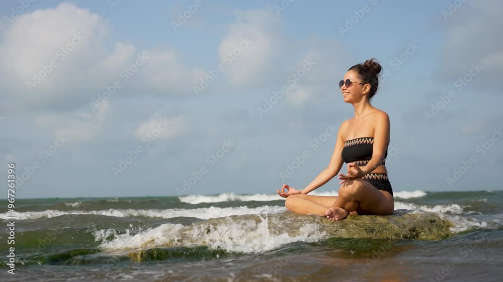 Young woman meditating at beach. Beautiful woman practicing lotus yoga pose on rocks at ocean Young woman meditating at beach. Beautiful woman practicing lotus yoga pose on rocks at ocean