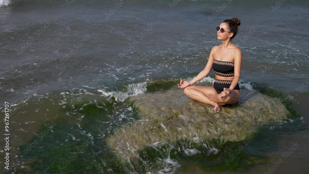 Young woman meditating at beach. Beautiful woman practicing lotus yoga pose on rocks at ocean Young woman meditating at beach. Beautiful woman practicing lotus yoga pose on rocks at ocean