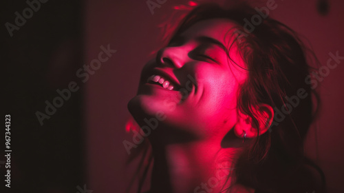 A woman smiling under red lighting in a dimly lit room