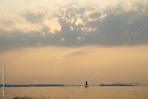 Young man standing on sup and paddling on water of calm lake, tranquil scenery.Boat and sunset. photo