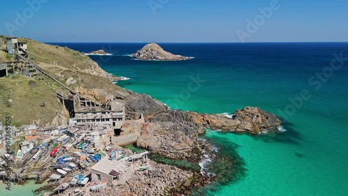 Ramshackle wooden homes and broken boats gather in clear turquoise green waters on edge of rocky beach below brooken home and observation deck photo