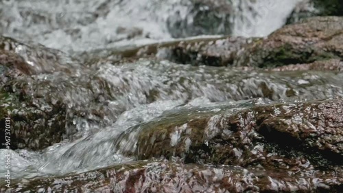 Close up water stream flowing through the rocks over the cascade in tropical rainforest during rainy season. Natural conservation.