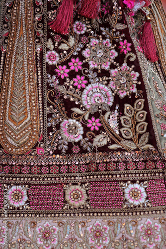A close-up of intricate floral embroidery on a rich fabric, featuring vibrant pink and gold threadwork. The detailed craftsmanship showcases traditional Indian design elements, adding elegance.