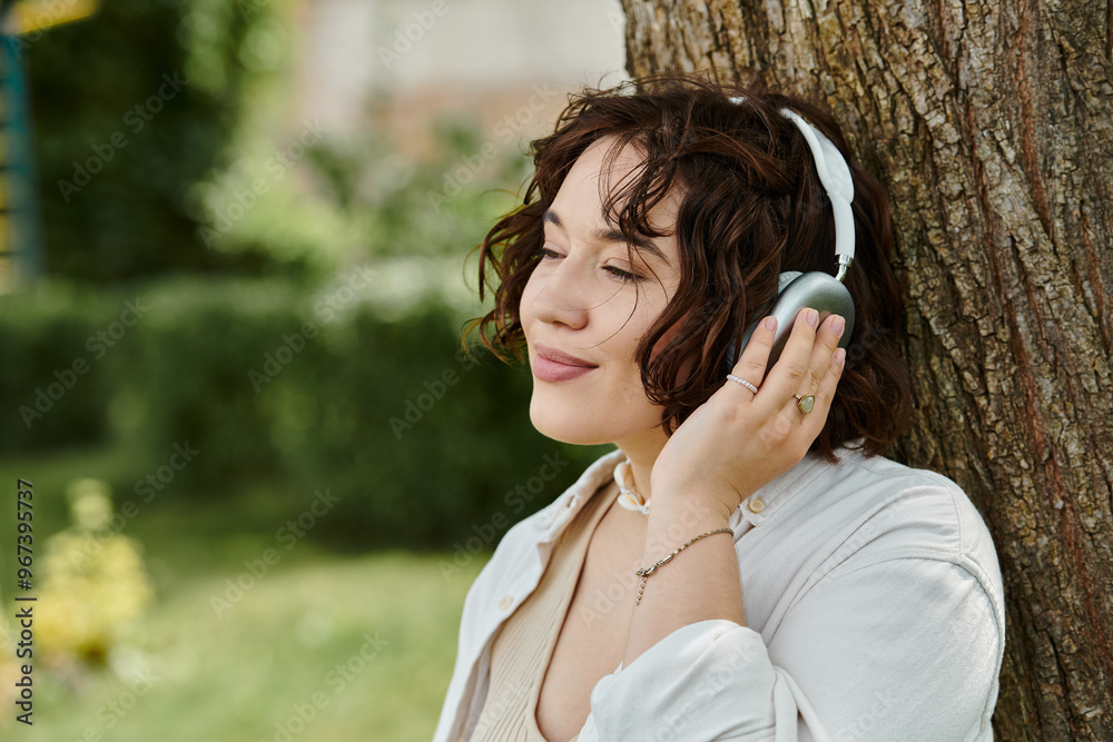 A young woman in a white shirt relaxes under a tree, soaking in summer warmth while listening to music. A young woman in a white shirt relaxes under a tree, soaking in summer warmth while listening to music.