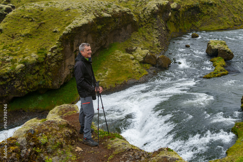 Man hiking by Icelandic waterfall in mossy canyon
