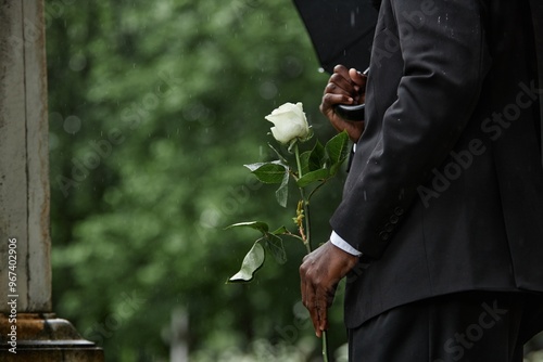 Картината върху платно Cropped shot of Black man in funeral black suit holding white rose in memory of