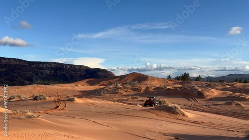 An ATV drives along the colorful, rippled Coral Pink Sand Dunes in Utah. Clouds move through the sky as the sun begins to set over the stunning desert landscape - USA