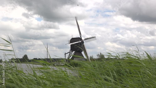 Historic windmill in Kinderdijk in the Netherlands on the waterfront. Cloudy day in summer. Reed grass in the foreground. photo