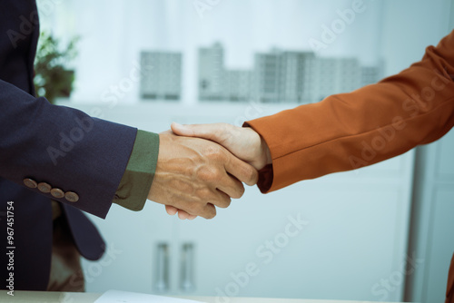  A businessman shakes hands with a customer in the sales office after agreeing to sign a contract to buy and sell a condo building. They discuss loans and real estate investment opportunities.