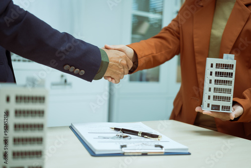  A businessman shakes hands with a customer in the sales office after agreeing to sign a contract to buy and sell a condo building. They discuss loans and real estate investment opportunities.