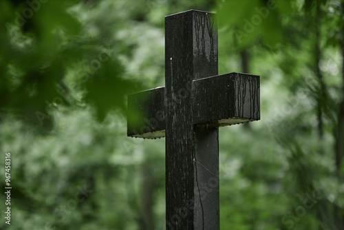 Shot through green leaves of granite memorial cross dripping with raindrops standing solemnly on grave in peaceful cemetery shaded by old tall trees, copy space