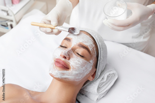 Beautician hand applying cosmetic mask on female face, lady client having skincare procedure in beauty salon. Concept of skincare and facial treatment photo