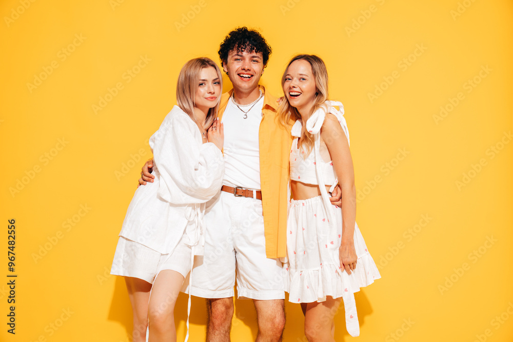 Group of young three stylish friends posing in studio. Fashion man and two cute female dressed in casual summer clothes. Smiling models having fun. Cheerful women and guy near yellow wall Group of young three stylish friends posing in studio. Fashion man and two cute female dressed in casual summer clothes. Smiling models having fun. Cheerful women and guy near yellow wall