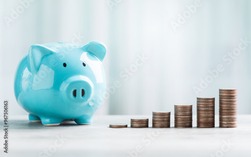 A blue piggy bank and stack of coins are neatly arranged on a table against a bright white background. The image represents the concept of saving money for the future. photo