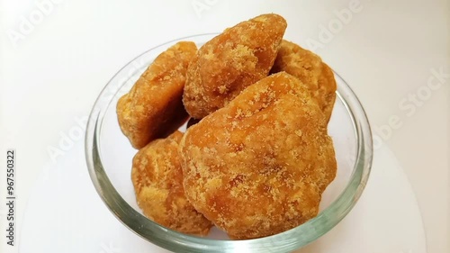 Organic Jaggery or Gur pieces in a glass bowl rotating against a clean white background, isolated. Brown cane sugar pieces in glass bowl isolated photo