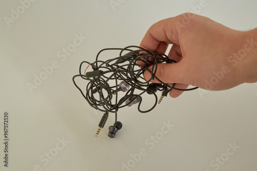 Hand trying to untangle tangled black thin wires from phone headphones, hand holding tangled wires, white background close-up photo