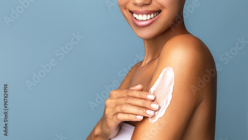 Photos A close-up of a smiling  african woman applying body skin care lotion to her shoulder