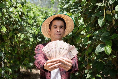 Man smiling and proudly displaying a fan of money in a green garden photo