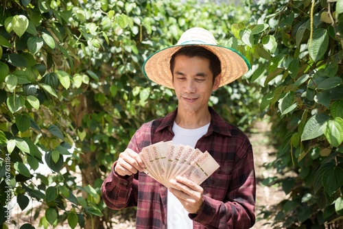 Farmer holding a fan of cash notes in a green garden with a satisfied expression photo