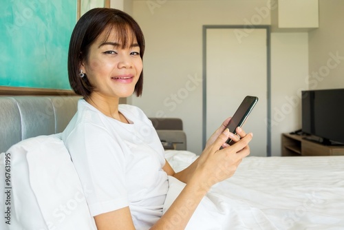 A woman looking at her smartphone while sitting on a hospital bed.