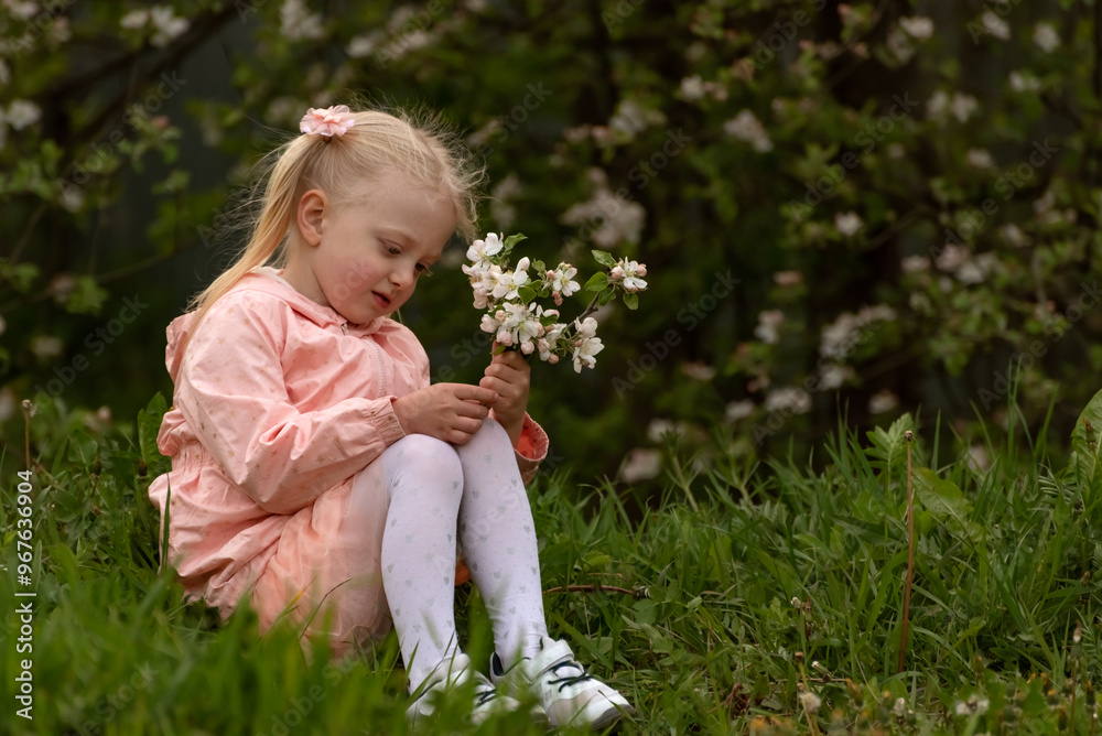 Girl of 4-5 year in pink dress sits on the grass with bouquet of flowers. Blonde child with two ponytails in spring in flowering garden. Girl of 4-5 year in pink dress sits on the grass with bouquet of flowers. Blonde child with two ponytails in spring in flowering garden.