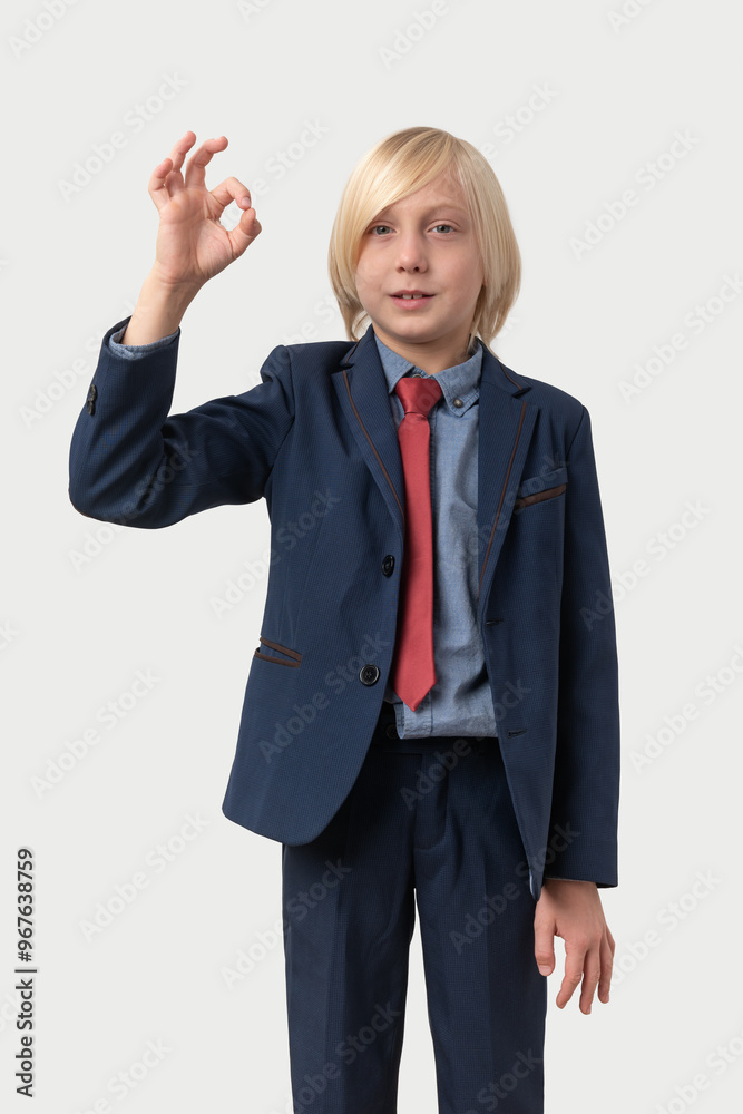 Young Caucasian boy in blue suit showing ok sign and looking at camera. Isolated on white background. Young Caucasian boy in blue suit showing ok sign and looking at camera. Isolated on white background.