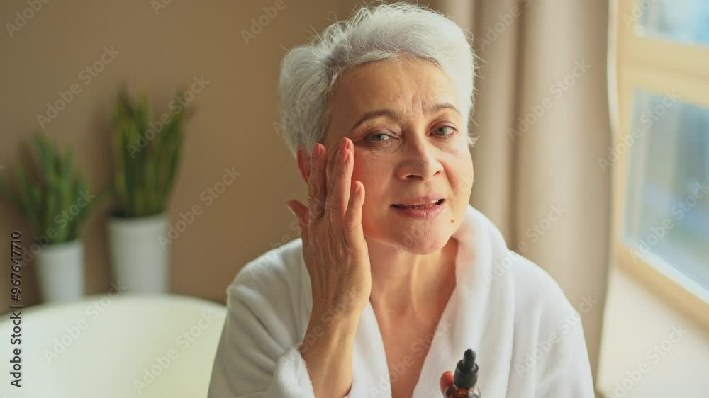 Woman applying natural drops cosmetics oil to face skin. Mature adult old woman applying nourishing anti age serum with pipette doing daily beauty routine. Senior woman gets kin scare facial treatment Woman applying natural drops cosmetics oil to face skin. Mature adult old woman applying nourishing anti age serum with pipette doing daily beauty routine. Senior woman gets kin scare facial treatment